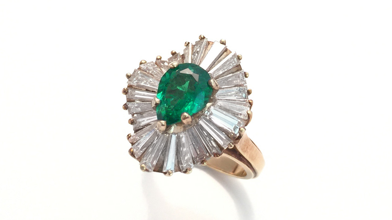 This emerald ring in a yellow gold mounting with tapered baguette diamonds is from the GIA Collection and was photographed with a mobile phone. It was photographed on a white tile background using museum wax to hold the ring up. Diffusion paper and reflector cards were used to light up the gems. Photo by Robert Weldon and Denise Conrad / GIA.